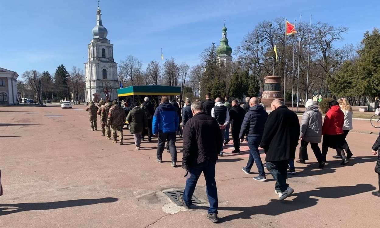 Траурна колона з Героєм "на щиті" іде площею, на якій не приспущені прапори на знак жалоби  