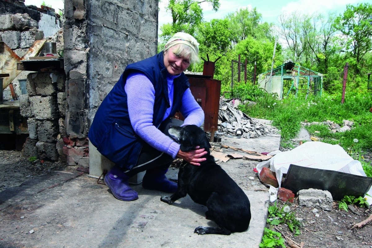 Ірина Горбонос на порозі свого будинку, який повністю зруйнований після обстрілів росіян. Видніється також знівечена тепличка господарів