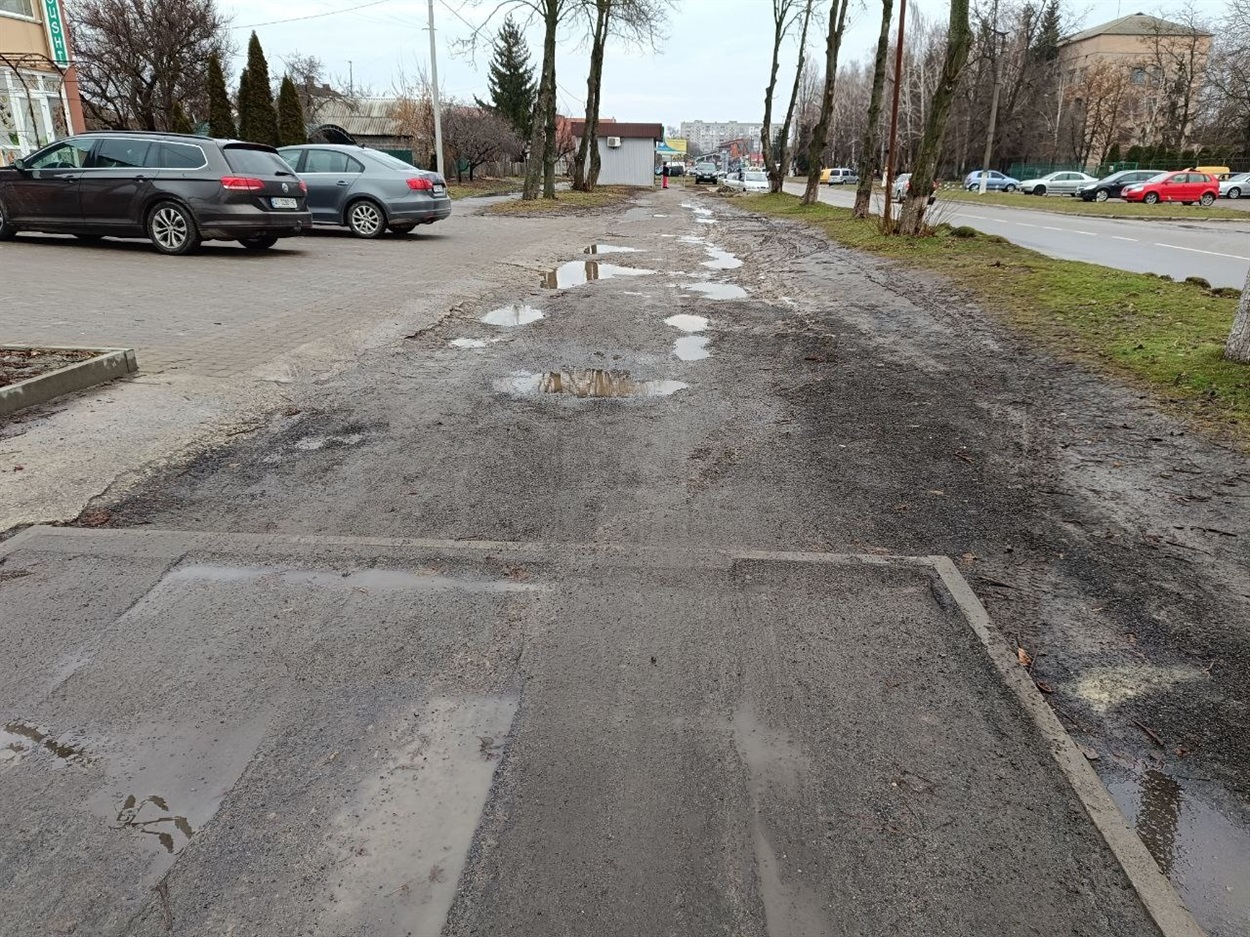 Новий тротуар розпочинається насправді не від магазину "Рибачок" - він видніється попереду за кількадесятків метрів, на зупинці громадського транспорту