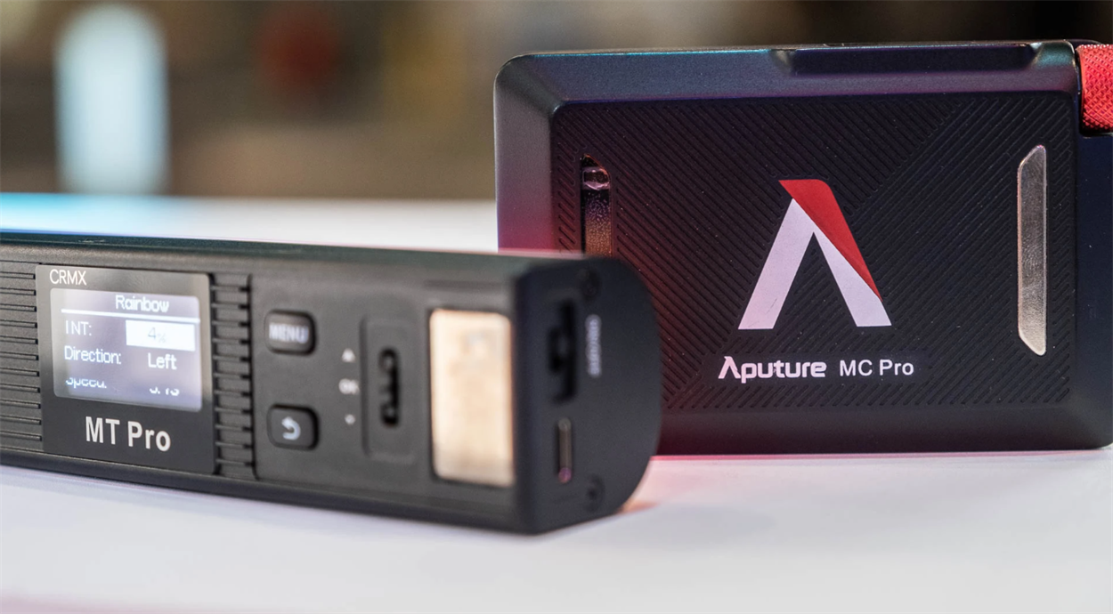 Контролер Aputure MT Pro з написом CRMX на екрані поруч із задньою панеллю Aputure MC Pro на світлому столі.